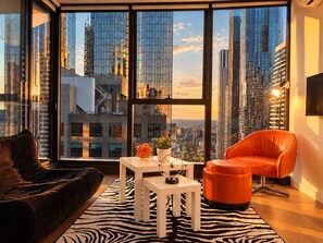 A modern living room with a large window, a zebra-patterned rug, a white coffee table, a red chair, and a black sofa. - Future Past CBD Views & Balcony (Melbourne)