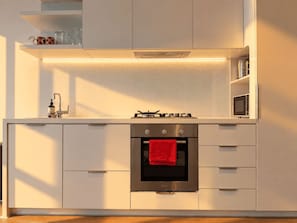 A modern kitchen with a built-in oven, a gas stove, and a microwave. - Future Past CBD Views & Balcony (Melbourne)
