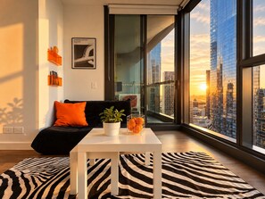 A modern living room with a black sofa, orange cushions, a white coffee table, and a zebra-patterned rug. - Future Past CBD Views & Balcony (Melbourne)