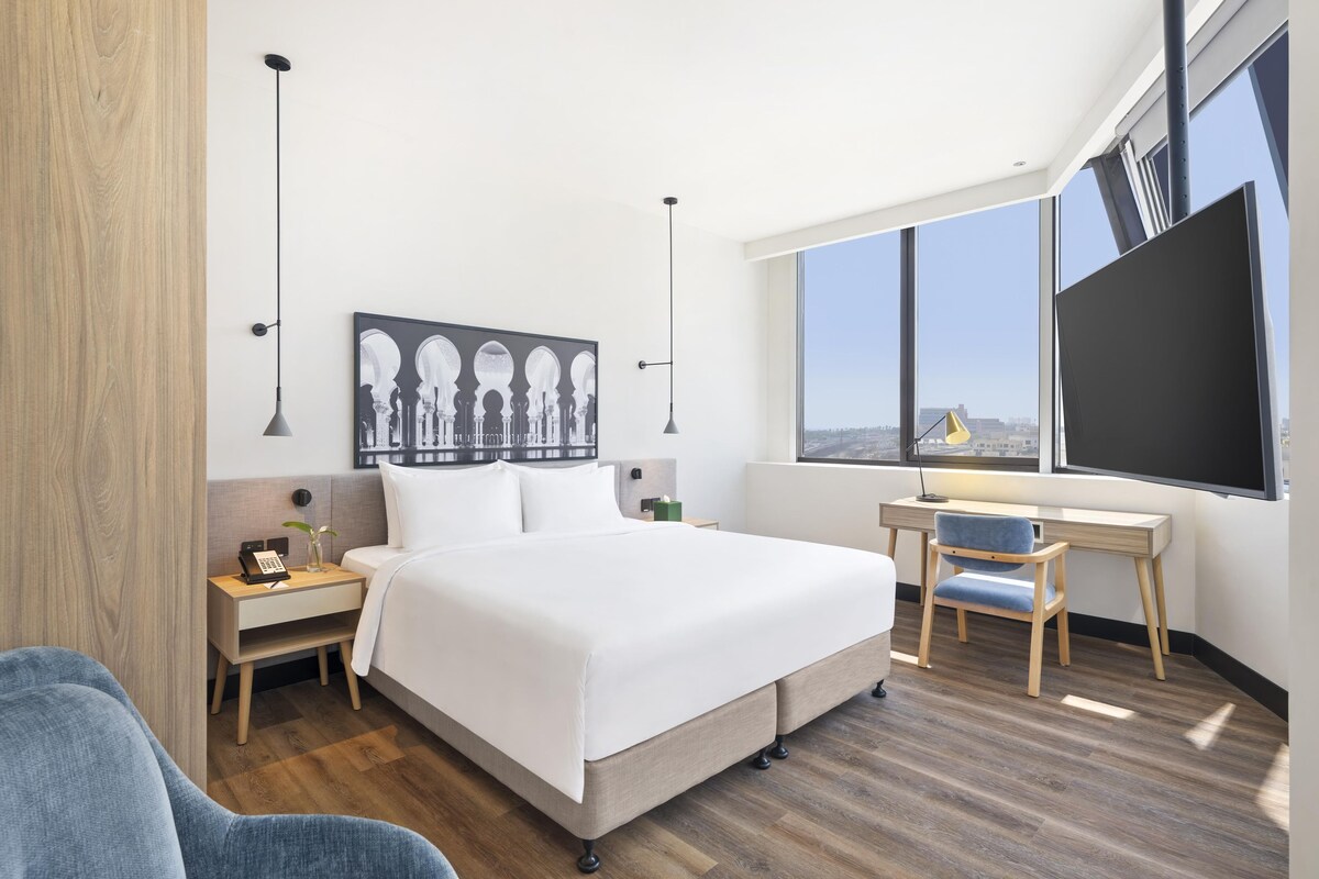 A modern hotel room with a large bed, a desk, and a view of the city.