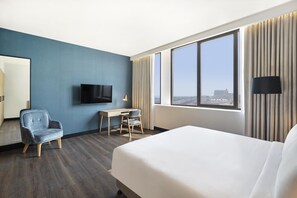 A hotel room with a bed, a desk, a chair, a TV, and a large window with a view.