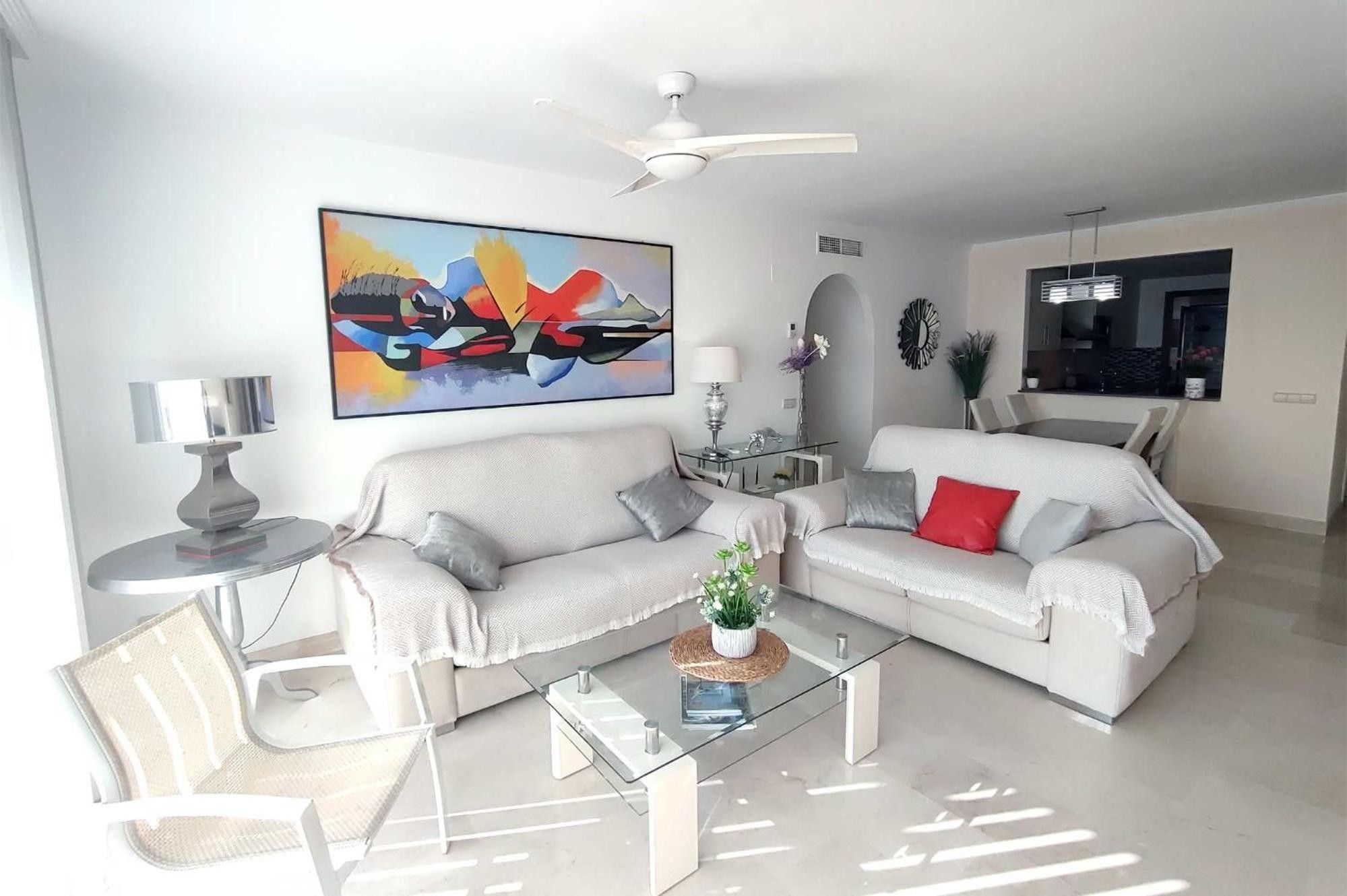 A modern living room with a sofa set, a glass coffee table, and a ceiling fan.