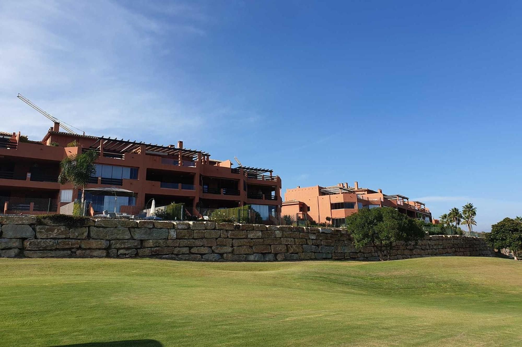 A multi-story hotel with a stone wall in front, a well-maintained lawn, and clear blue skies.