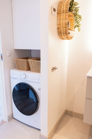 Ein kleiner Waschraum mit einer Waschmaschine mit Frontlader, einem Schrank und einem Korbwäscheschrank an der Wand.