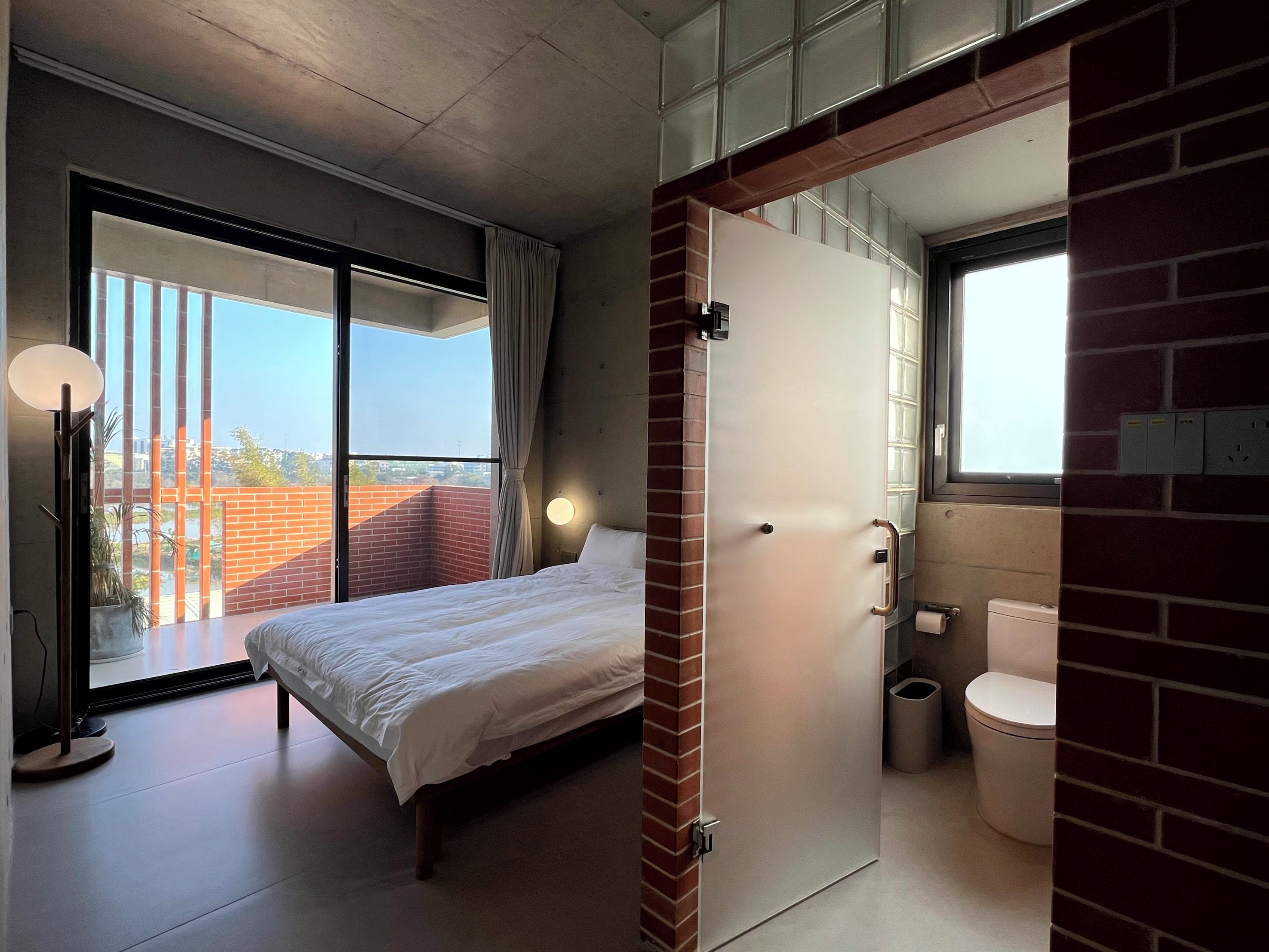Una habitación de hotel con cama, baño, ventana grande y vista a la ciudad.