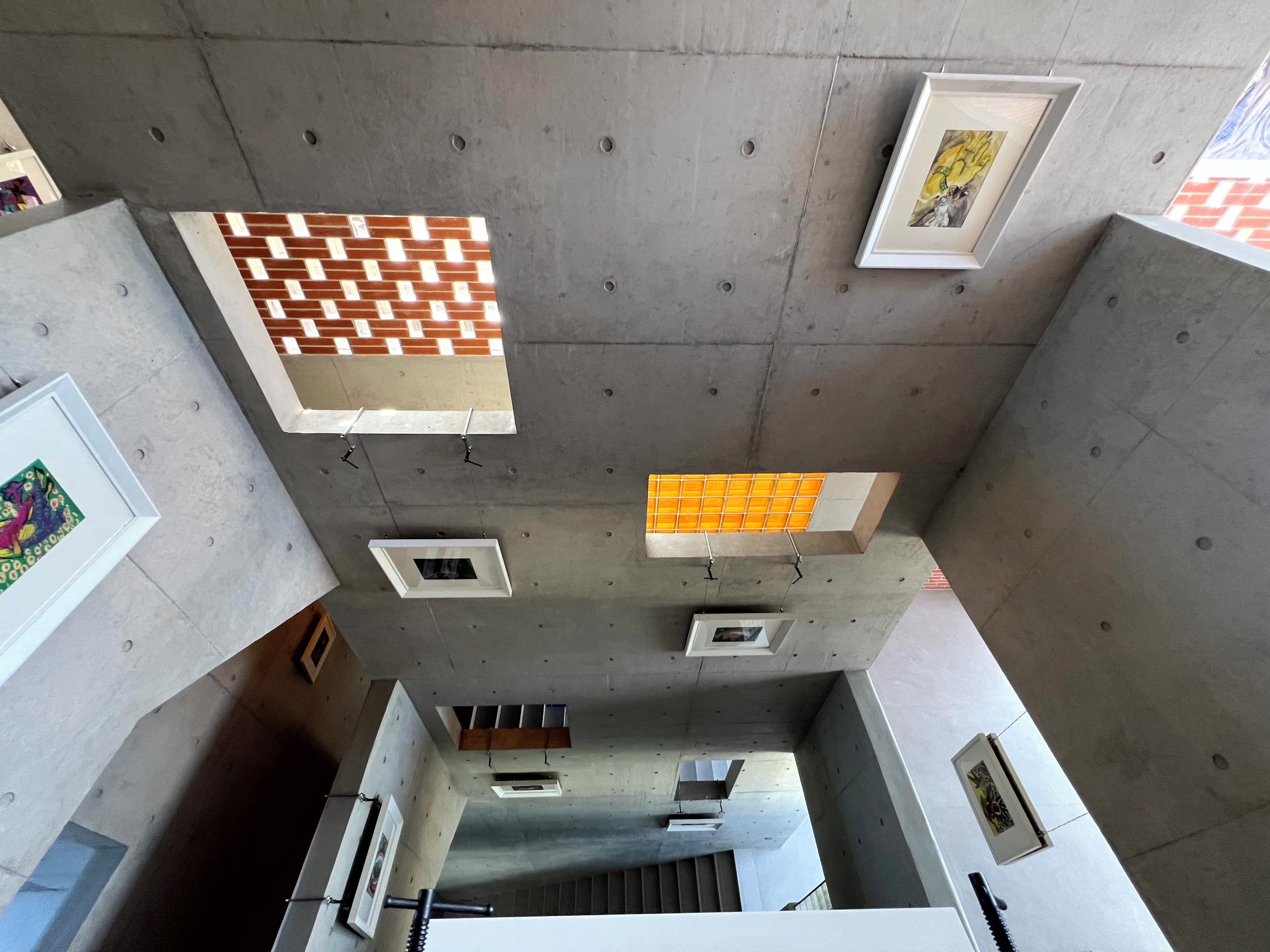Un intérieur moderne avec un plafond en béton, de nombreux tableaux encadrés et un escalier menant à un autre niveau.