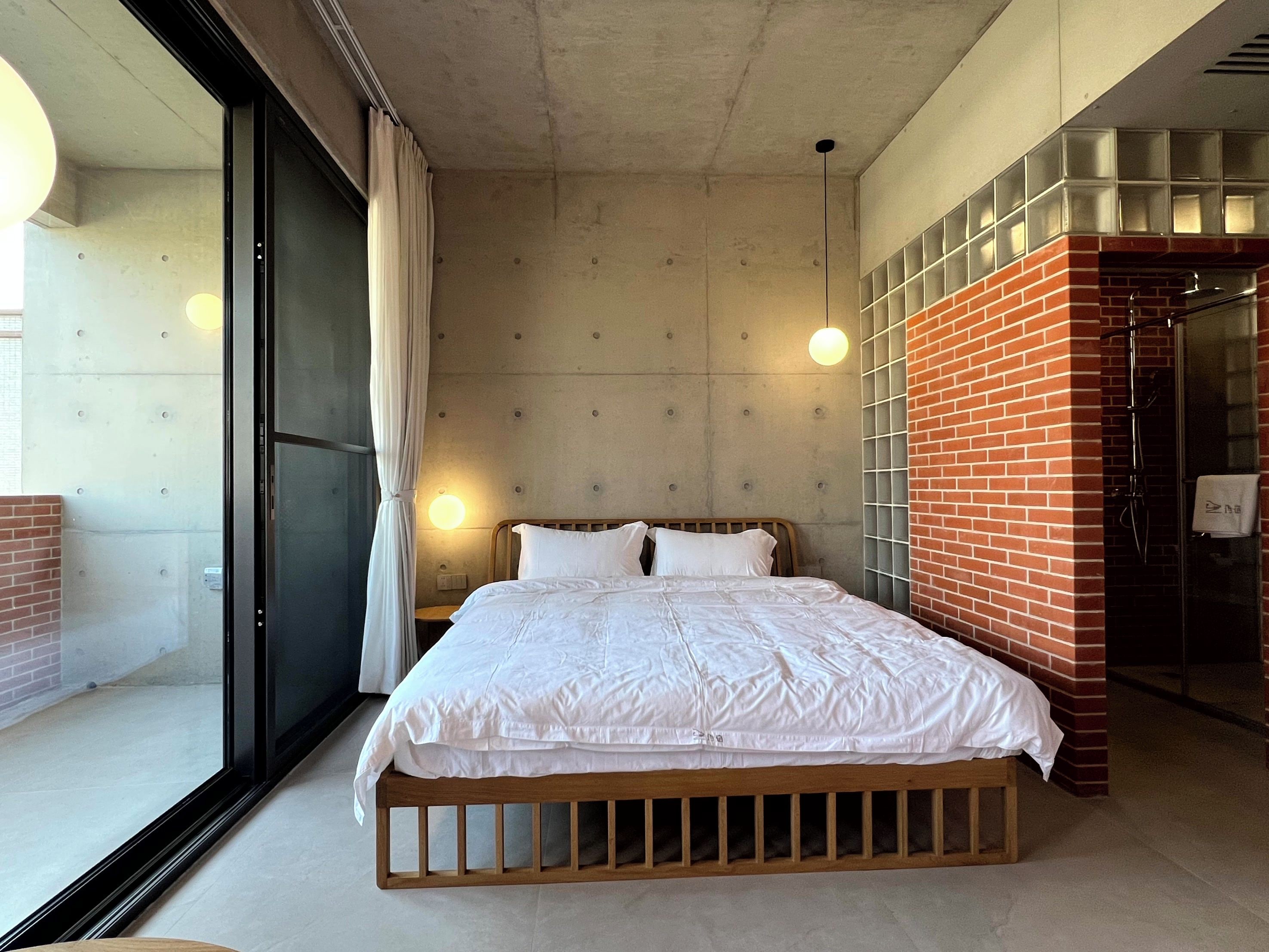 Quarto moderno com uma cama grande, porta de vidro e parede de tijolos decorativa.