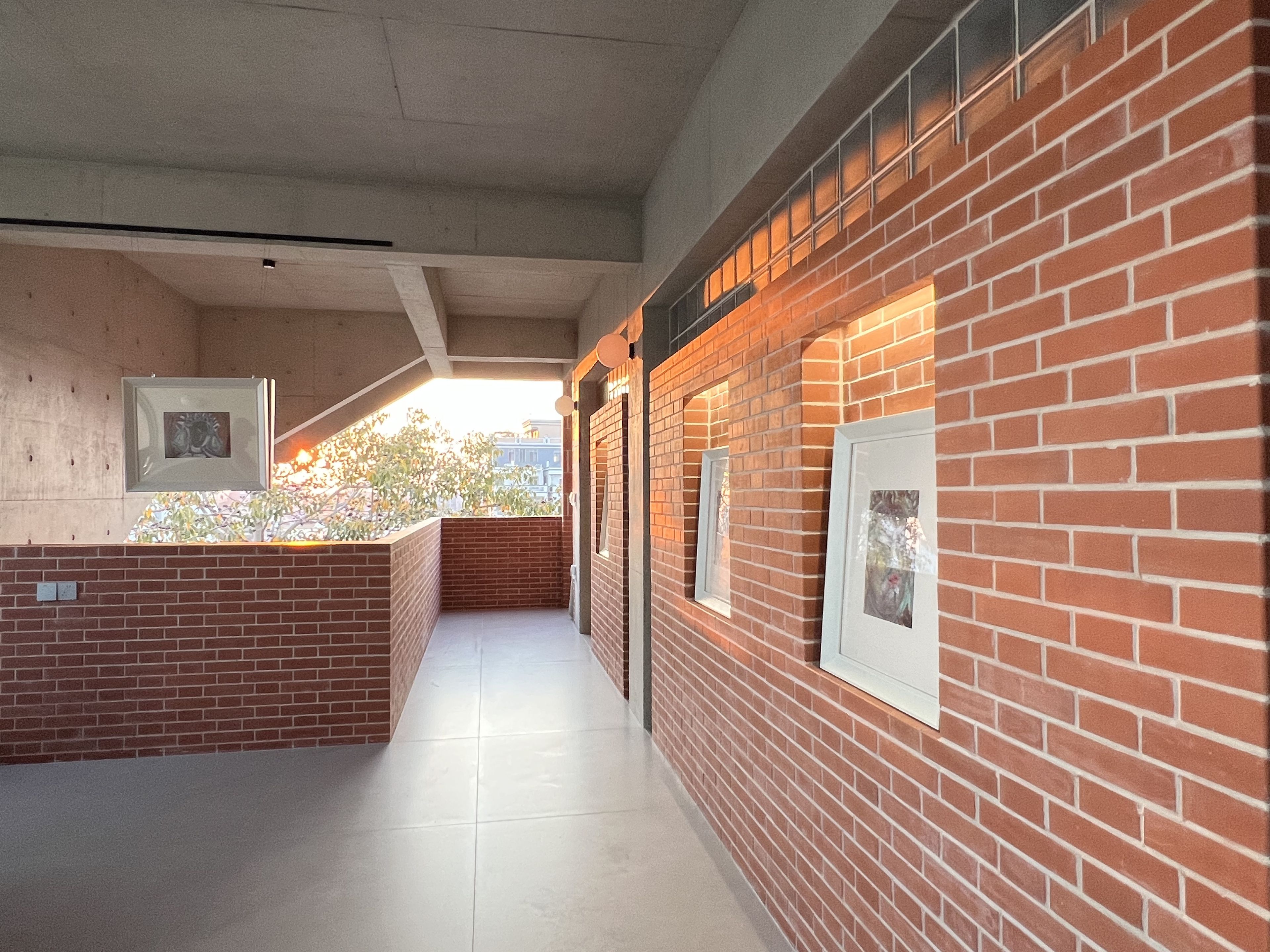A corridor with brick walls, framed pictures, and a tiled floor.