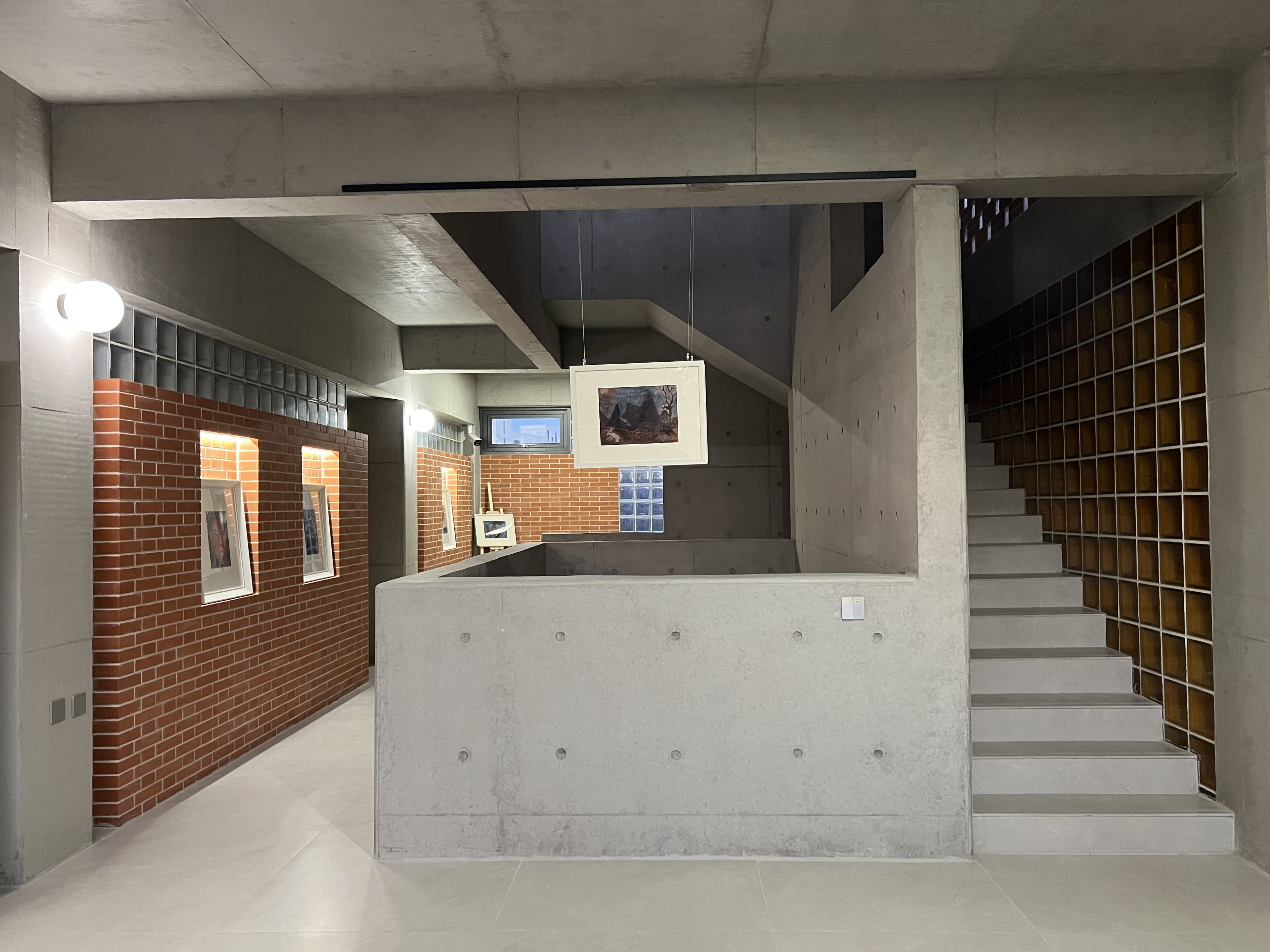 A modern interior with a staircase, concrete walls, and a brick wall with framed pictures.