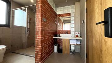 A bathroom with a glass shower enclosure, a white sink, and a wooden door.
