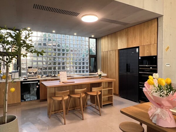Une cuisine moderne avec un îlot central, des chaises en bois, un réfrigérateur noir et une fenêtre donnant sur un paysage verdoyant.