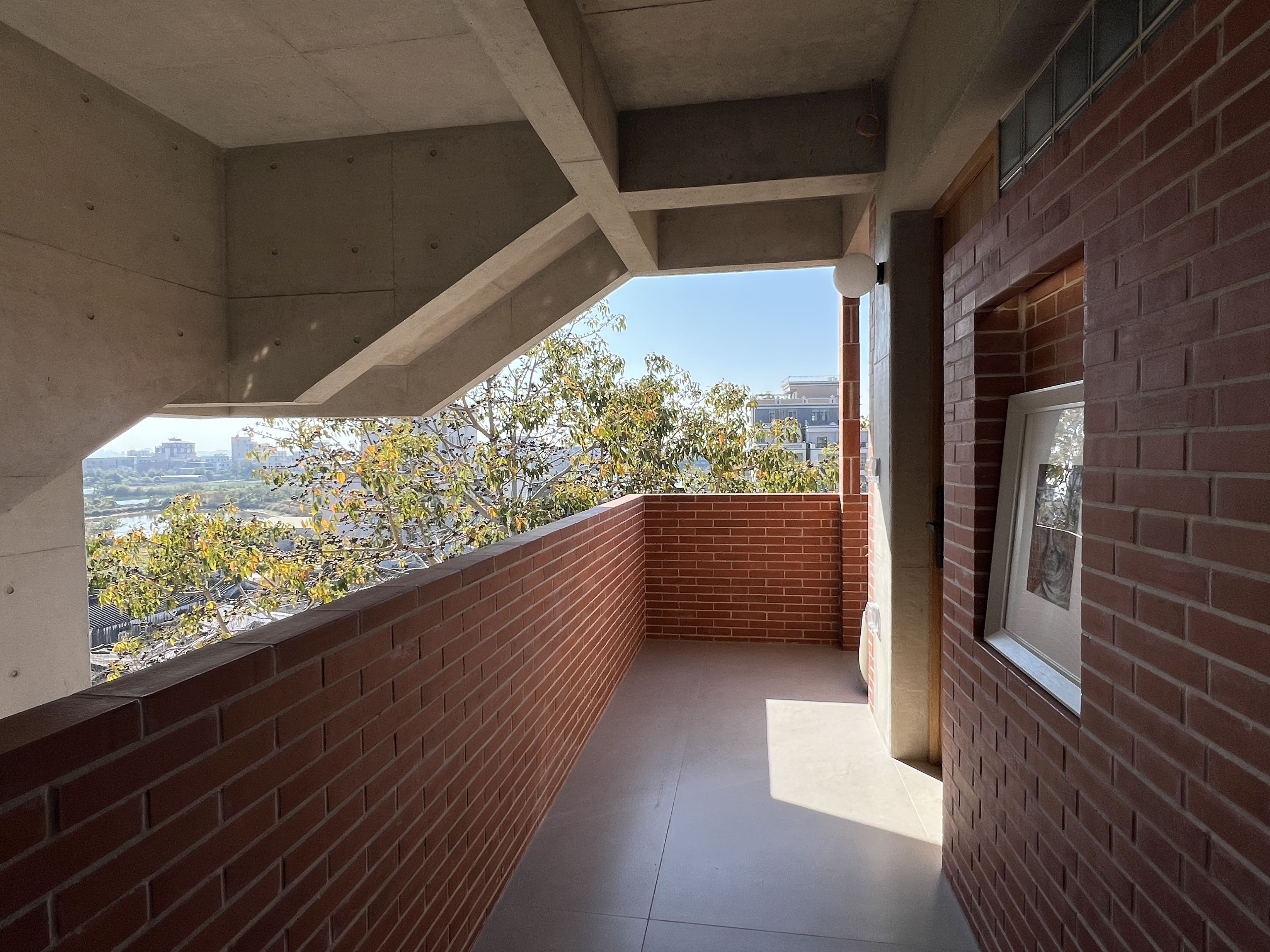 A balcony with a view of a river and trees, a tiled floor, and a brick wall.