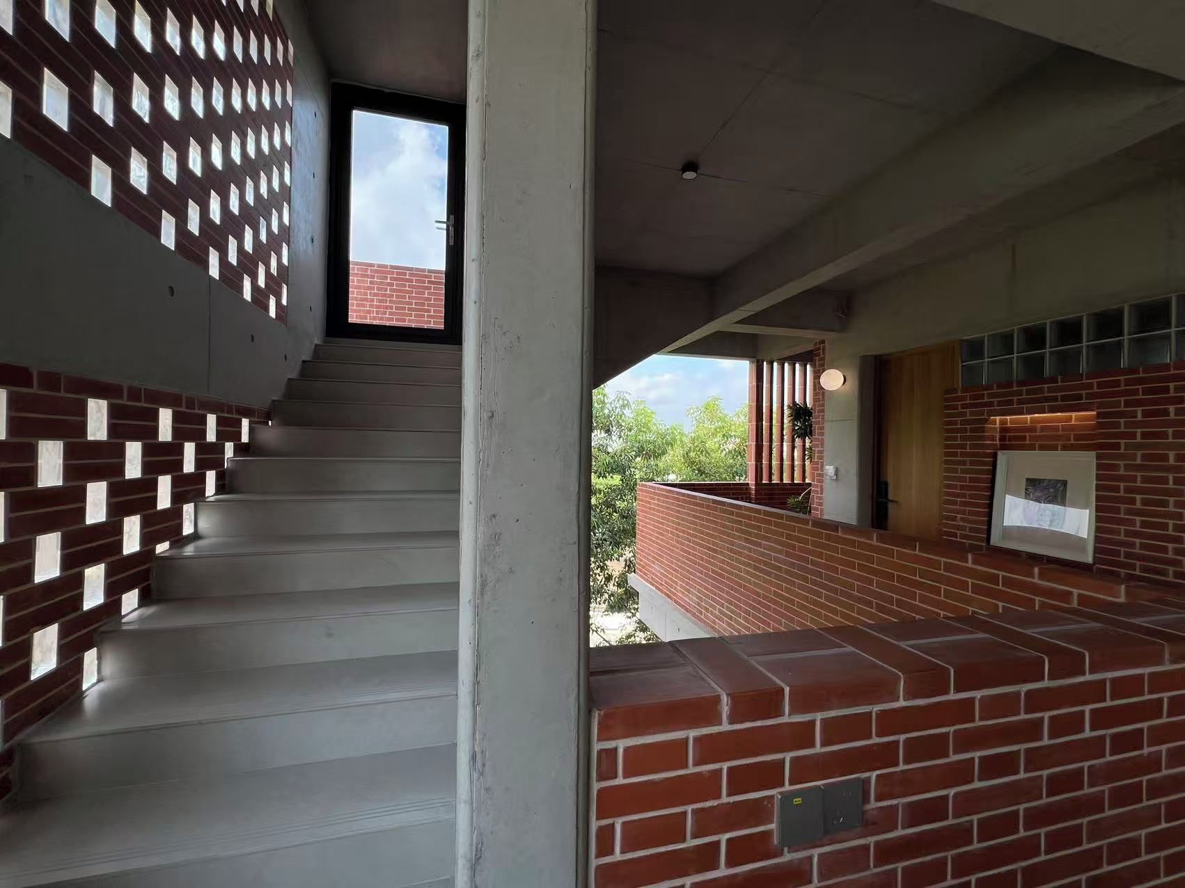 Una escalera con un muro de ladrillo a un lado y un muro blanco al otro, que conduce a un espacio exterior con un muro de ladrillo y una ventana.