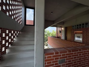 A staircase with a brick wall on one side and a white wall on the other, leading to an outdoor area with a brick wall and a window.