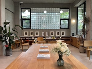 Une salle de conférence avec une longue table en bois, des chaises, un vase rempli de fleurs blanches et une bibliothèque contenant des livres et des photos encadrées.