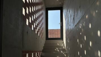A staircase with a brick wall on one side and a concrete wall on the other, leading to a door with a view of a brick building outside.
