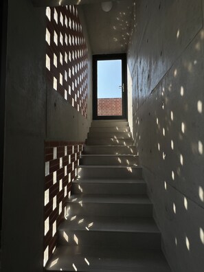 A staircase with a brick wall on one side and a concrete wall on the other, leading to a door with a view of a brick building outside.