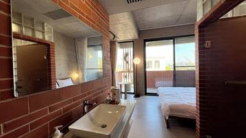 Een moderne badkamer met een grote spiegel, een rechthoekig wastafelmeubel en een bed met een witte dekbedovertrek.