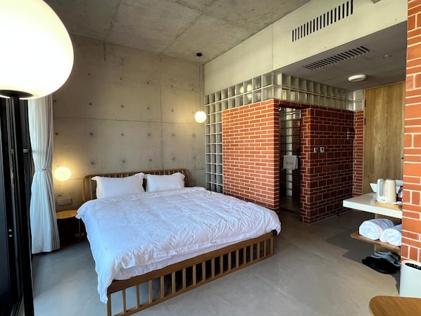 A hotel room with a bed, a nightstand, a lamp, a shower area, and a small table with towels.