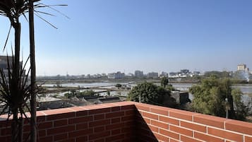 Vista desde un balcón con pared de ladrillo, sobre un paisaje urbano con edificios y un río.