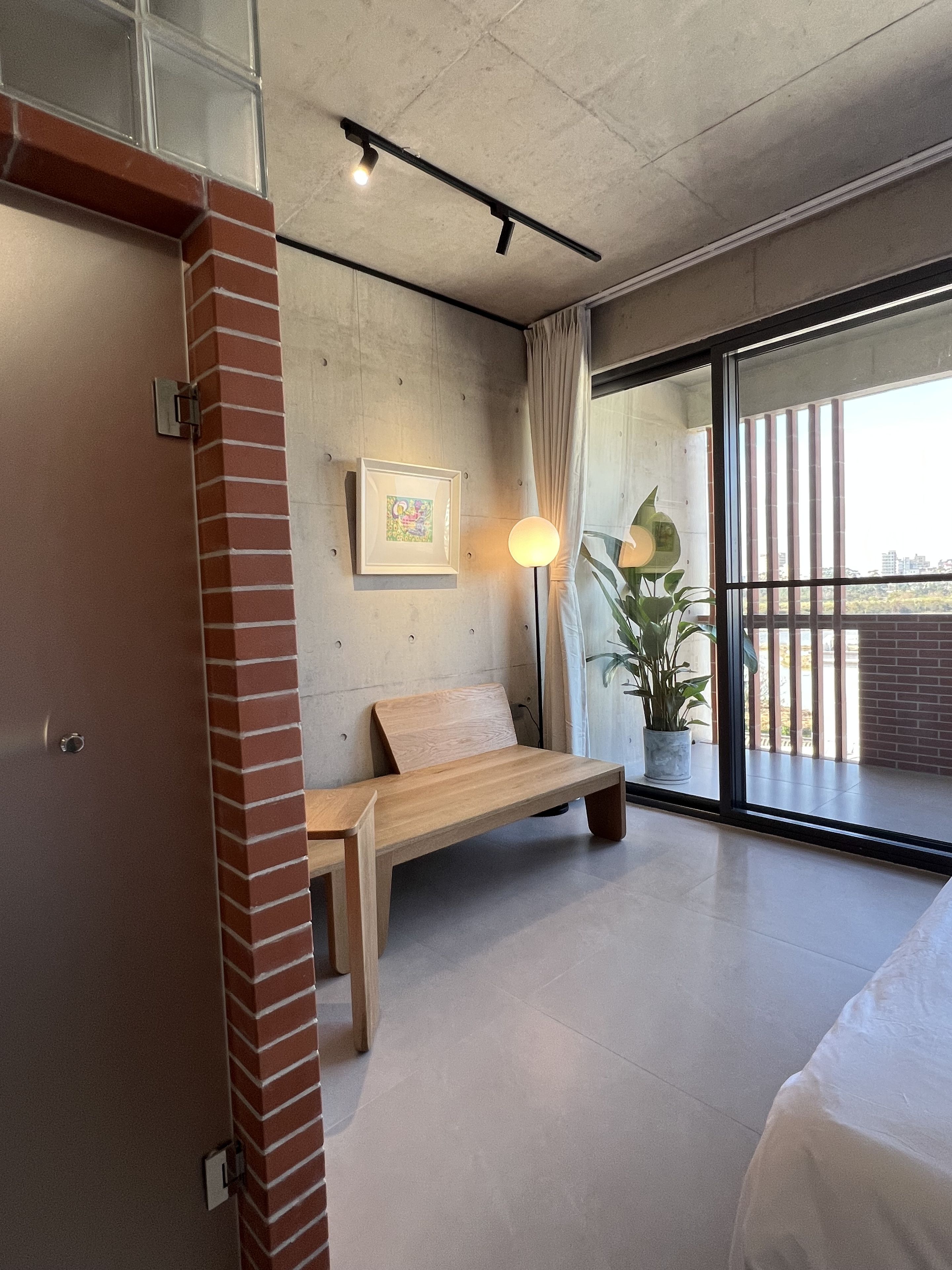 Una habitación moderna con un banco de madera, un cuadro enmarcado, una lámpara de pie y un ventanal con vistas.