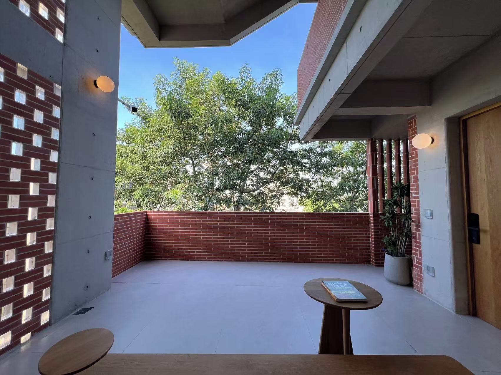 Un espacio exterior moderno con un muro de ladrillo, una mesa de madera con un libro y vistas a árboles.