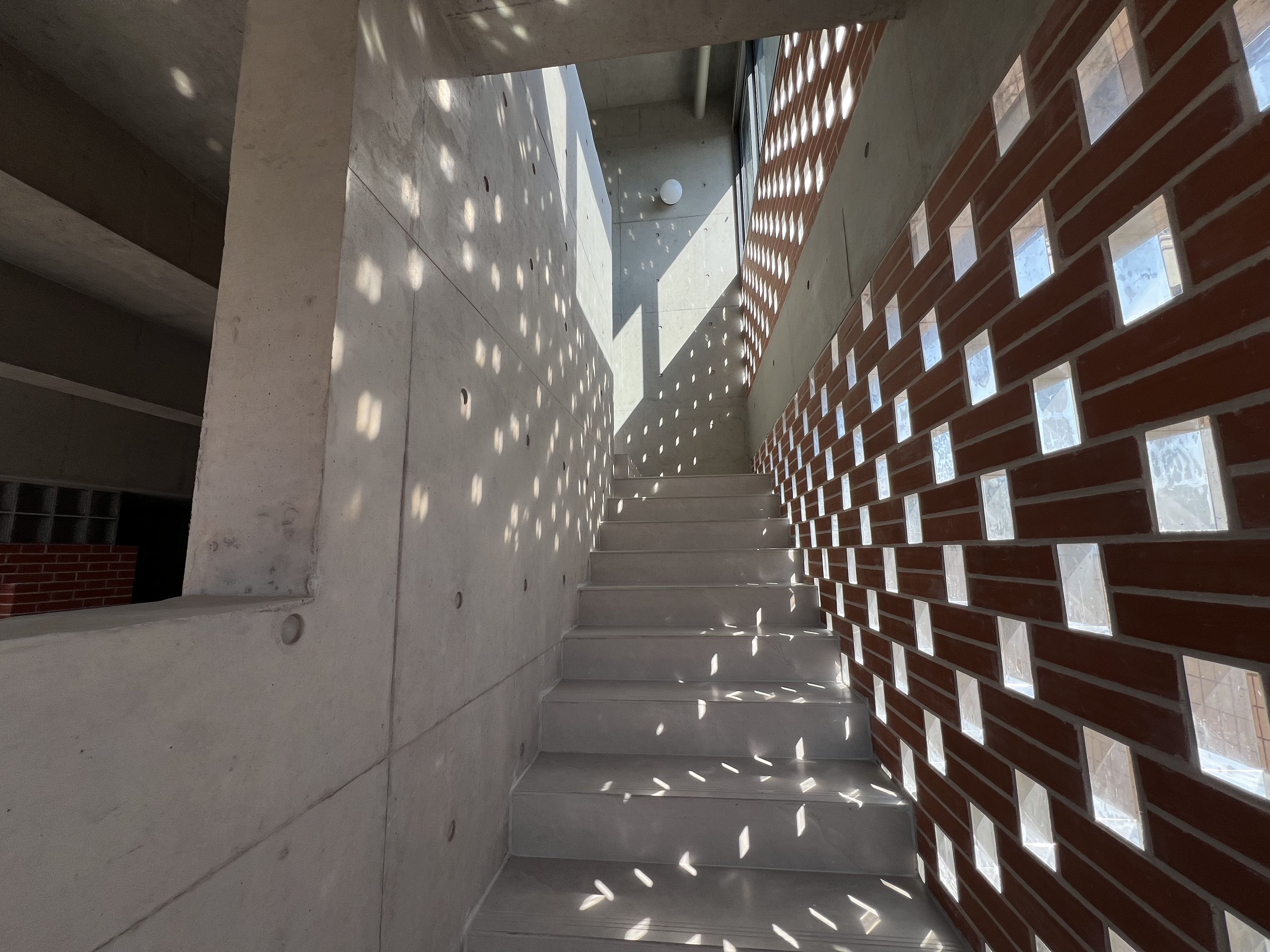 A staircase with a modern design, featuring a brick wall with square cutouts on the right side and a plain concrete wall on the left.