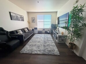 A living room with a sofa, a rug, a plant, and a wall-mounted TV. - Cozy 1-bedroom apartment in the heart of uptown Oakland with AC and gym access (Oakland)