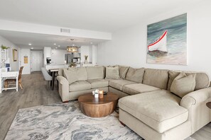 A modern living room with a sectional sofa, a round coffee table, and a painting of a sailboat on the wall. - Renovated Direct Oceanfront Island Club (Hilton Head)