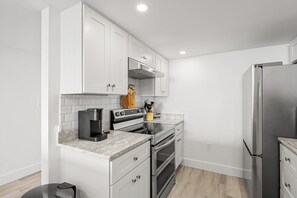 A modern kitchen with white cabinetry, a stainless steel refrigerator, a coffee maker, and an oven. - Renovated Direct Oceanfront Island Club (Hilton Head)
