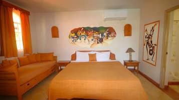 A hotel room with a large bed, a sofa, a painting on the wall, and an air conditioning unit.