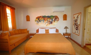 A hotel room with a large bed, a sofa, a painting on the wall, and an air conditioning unit. - Case Damare Madrugada (las terrenas)