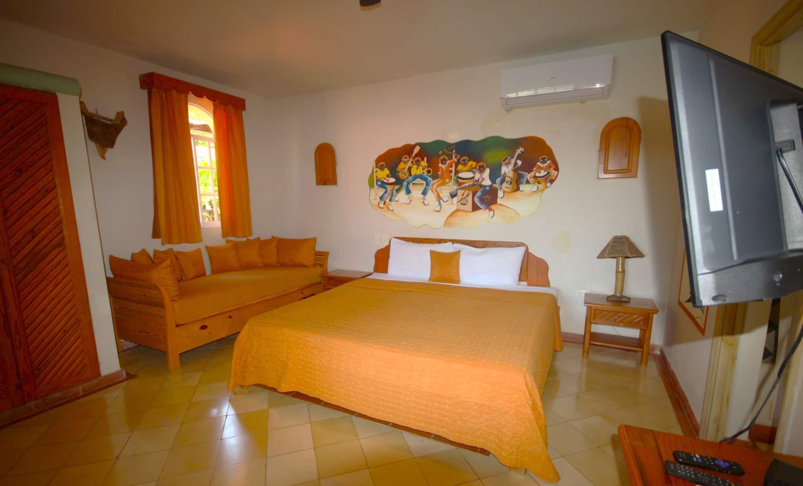 A hotel room with a bed, a sofa, a television, and a mural on the wall.