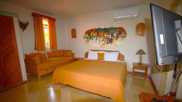 A hotel room with a bed, a sofa, a television, and a mural on the wall.