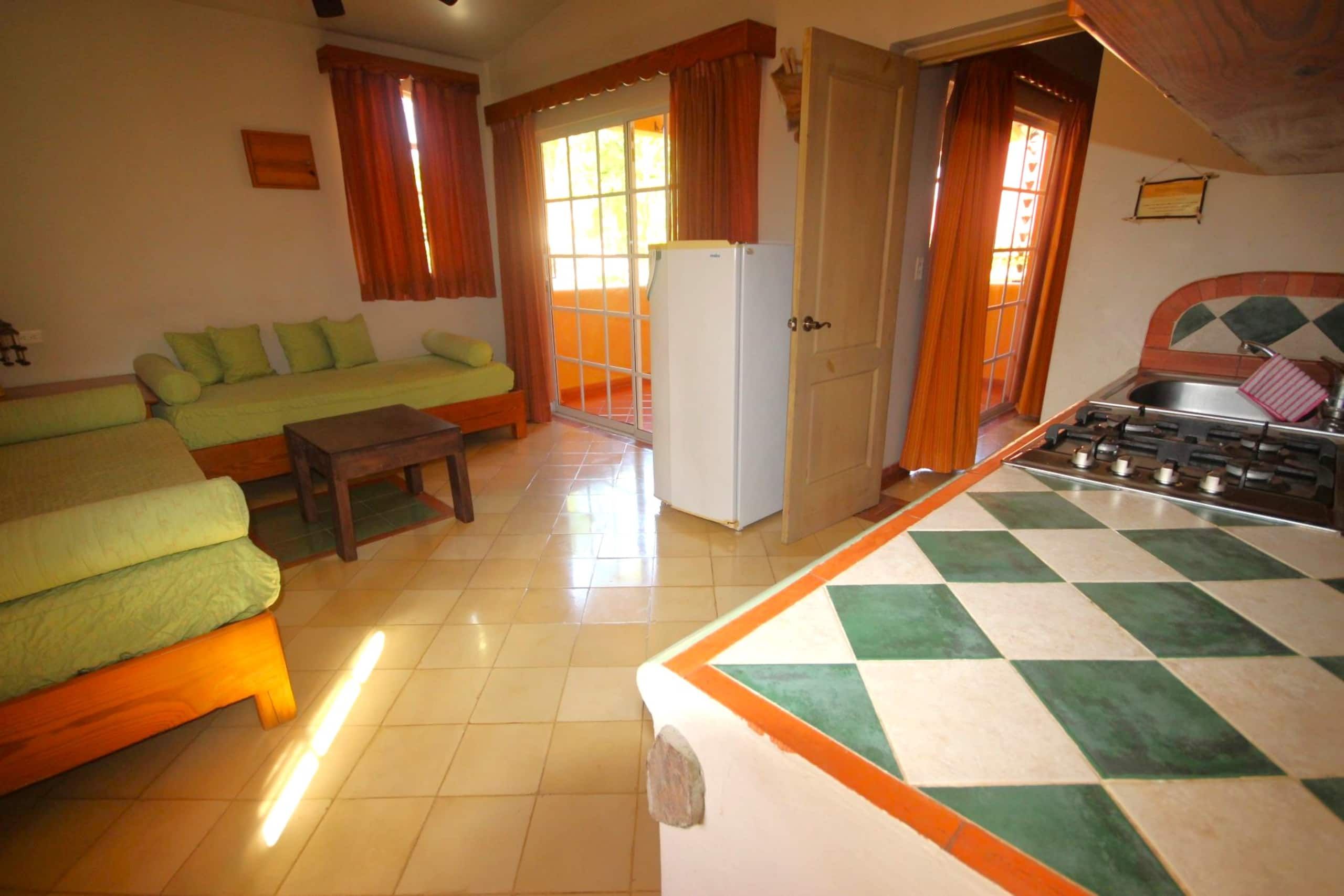 A compact living space with a sofa, a small table, a refrigerator, and a kitchen area with a tiled backsplash.