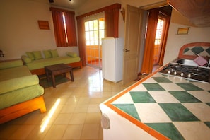 A compact living space with a sofa, a small table, a refrigerator, and a kitchen area with a tiled backsplash. - Case Damare Madrugada (las terrenas)