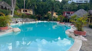 A swimming pool with a stone border, surrounded by tropical vegetation and buildings.