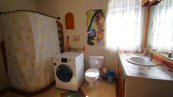Un baño con lavadora, inodoro, cortina de ducha y un espejo grande.