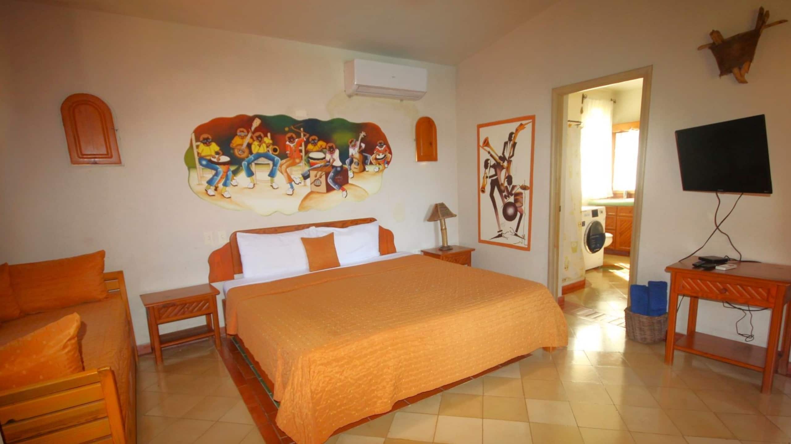 A hotel room with a large bed, a television, a painting, and a door leading to a bathroom.