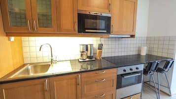 Eine kompakte Küche mit Holzschränken, einer Edelstahl-Spüle, einer Mikrowelle, einem Backofen und einer Kaffeemaschine.