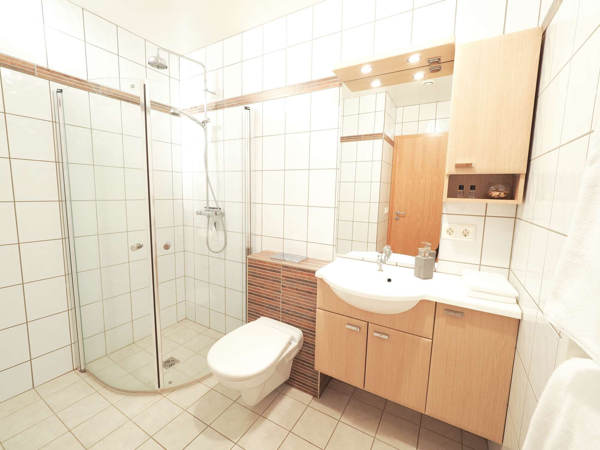 Ein modernes Badezimmer mit einer gläsernen Duschkabine, einer Toilette und einem Waschbecken mit Holzschrank.