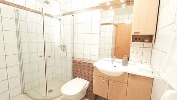 Ein modernes Badezimmer mit einer gläsernen Duschkabine, einer Toilette und einem Waschbecken mit Holzschrank.