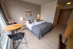 A hotel room with a bed, a small table with a lamp, a chair, and a painting on the wall.