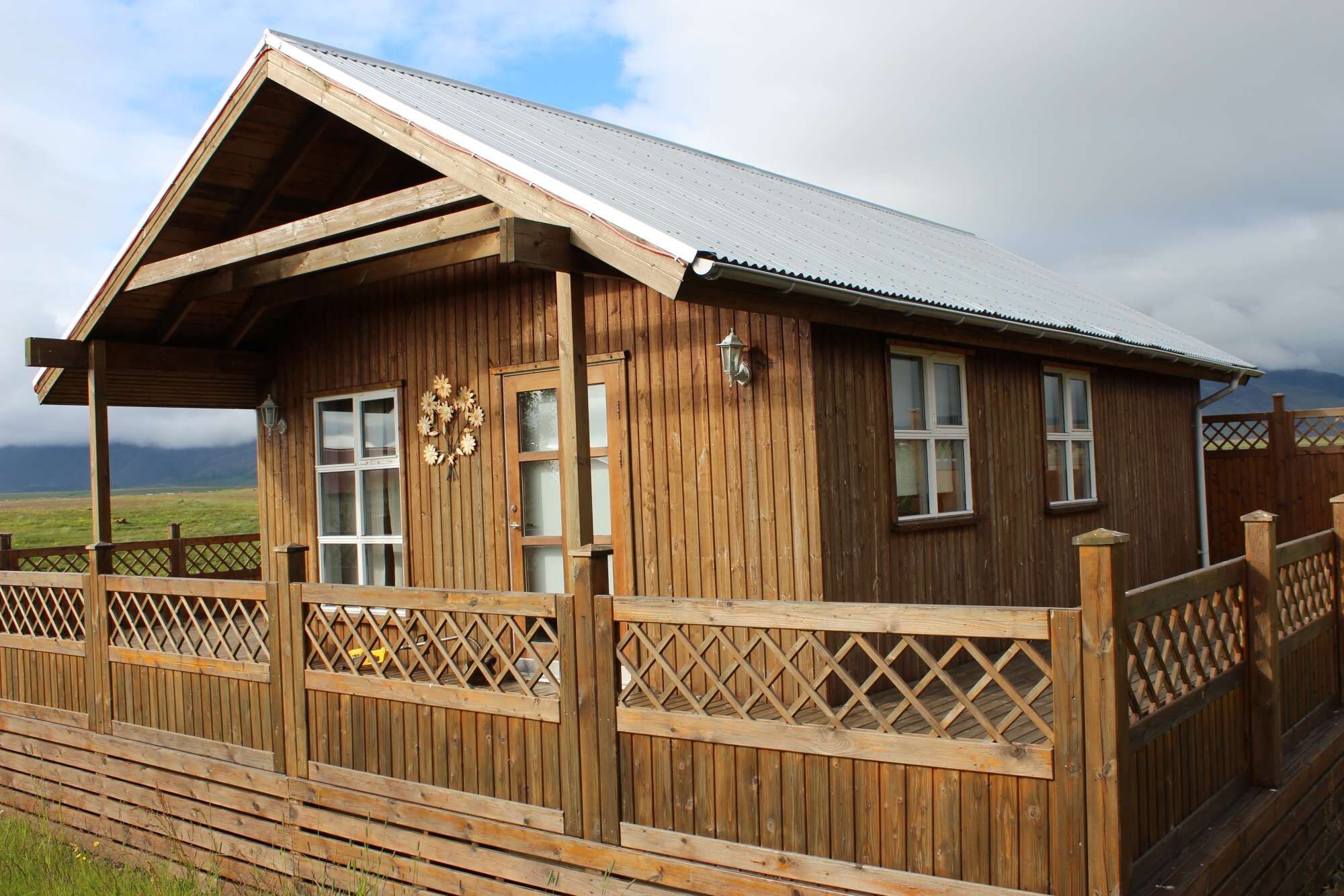 A wooden cabin with a sloped roof, a porch with lattice railings, and a decorative wall-mounted light fixture.