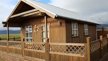 A wooden cabin with a sloped roof, a porch with lattice railings, and a decorative wall-mounted light fixture.