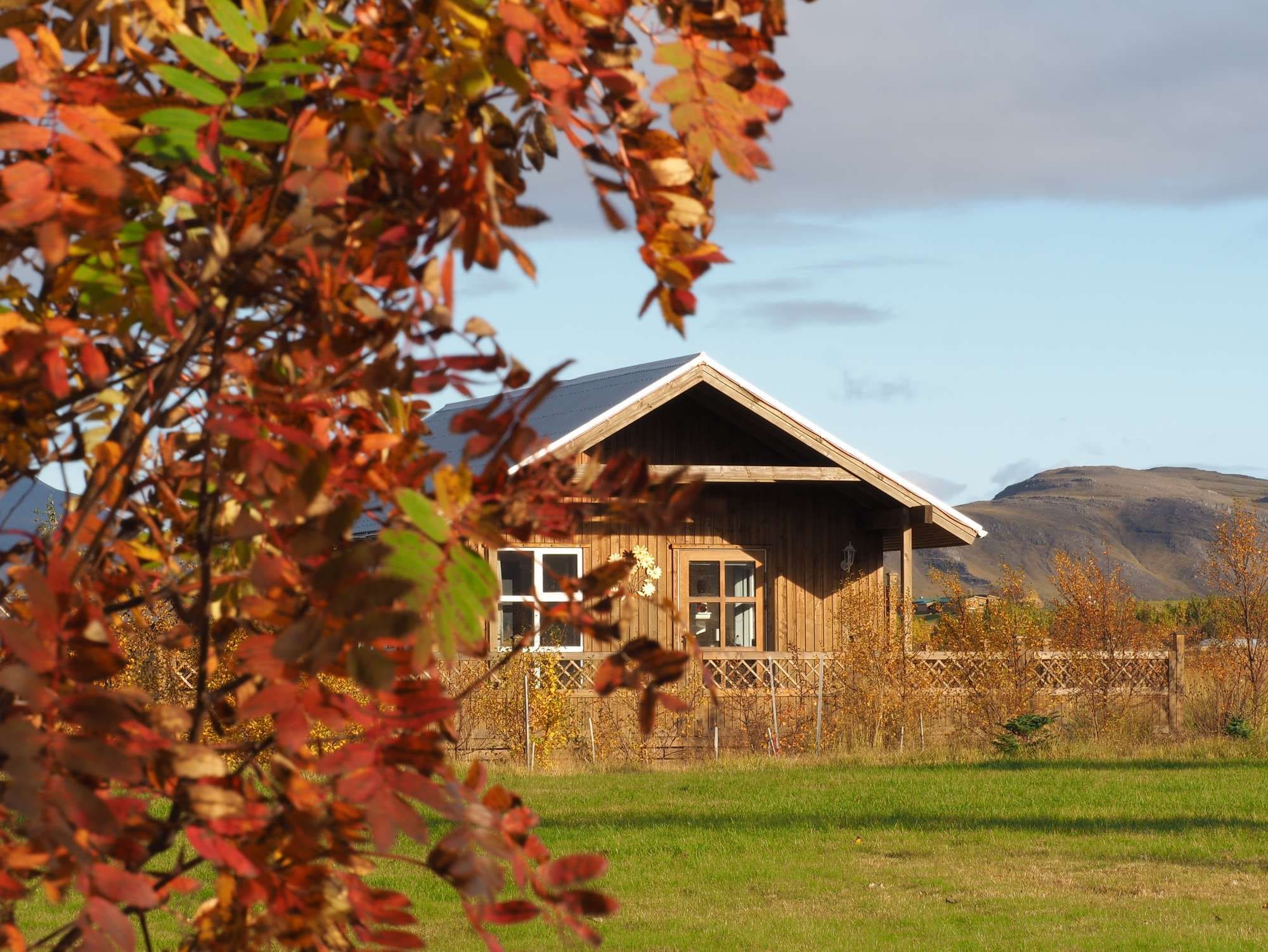Ein Holzhaus mit geneigtem Dach, umgeben von einem eingezäunten Hof und einem Berg im Hintergrund.