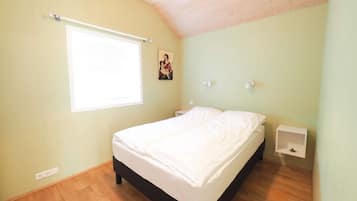 Ein Schlafzimmer mit einem Bett, einem Fenster mit Jalousien, einer Wandleuchte und einem kleinen Nachttisch.