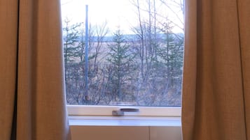A window with beige curtains, a radiator below, and a view of trees and a power pole outside.