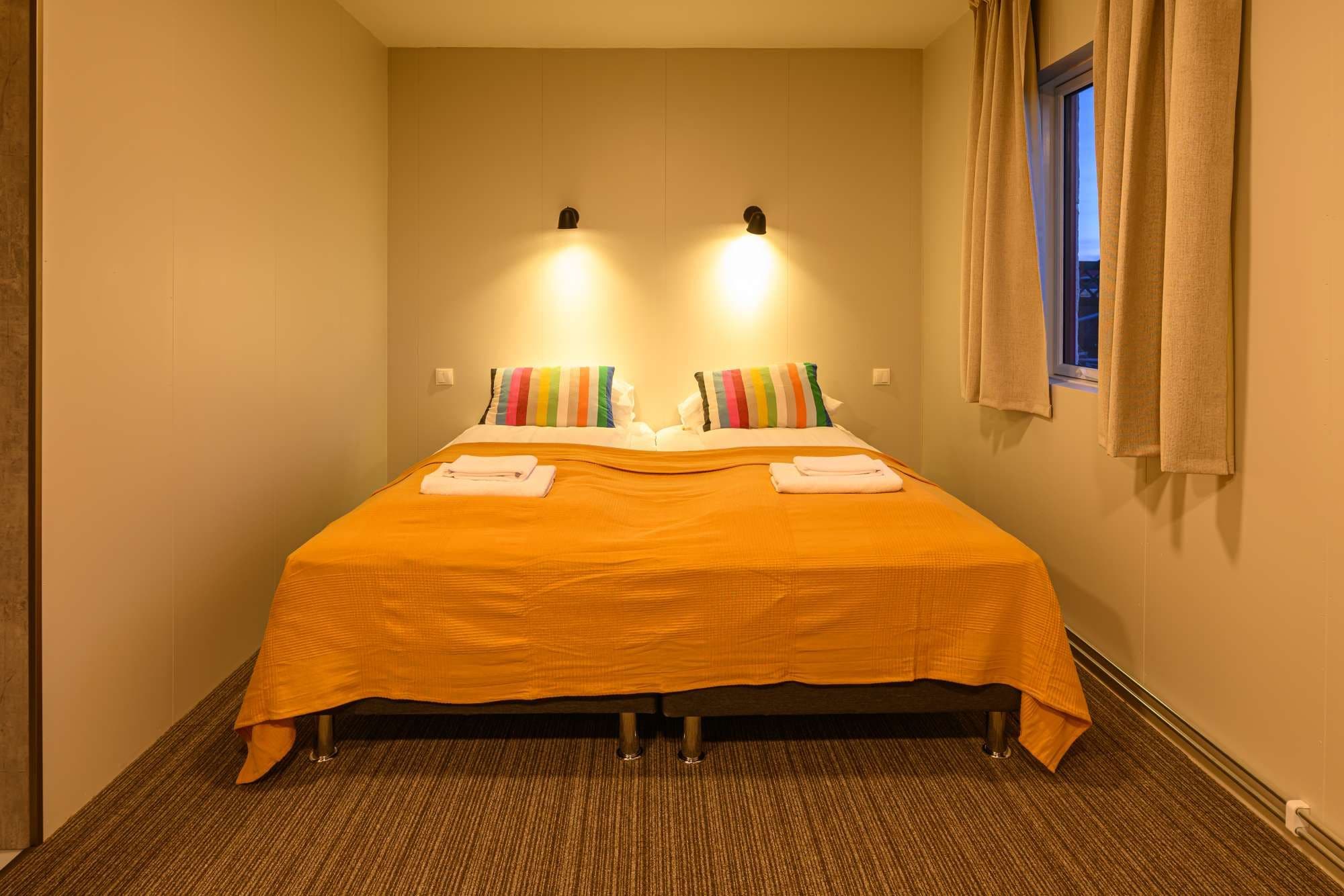 Ein Hotelzimmer mit einem Bett, zwei Wandleuchten, einem mit Vorhängen versehenen Fenster und einem Teppichboden.