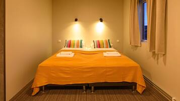Ein Hotelzimmer mit einem Bett, zwei Wandleuchten, einem mit Vorhängen versehenen Fenster und einem Teppichboden.